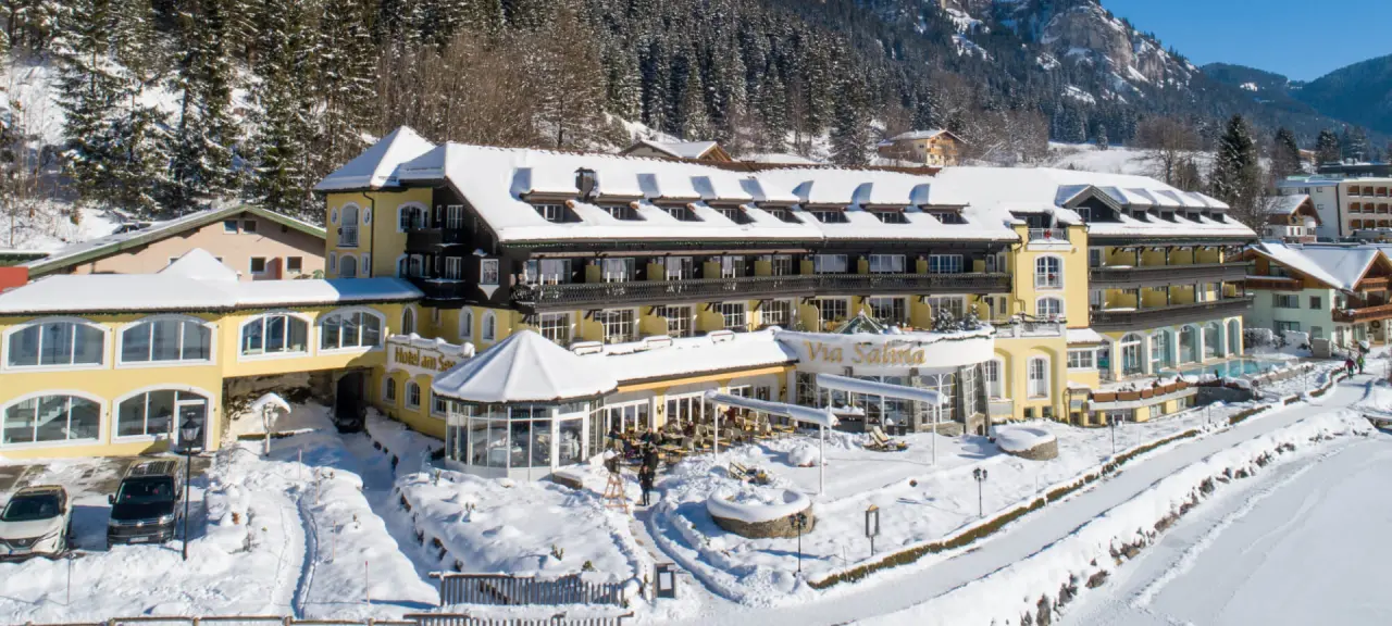 Hotel Via Salina im Winter mit verschneiter Fassade, Aussenpool und Bergpanorama in den Alpen.
