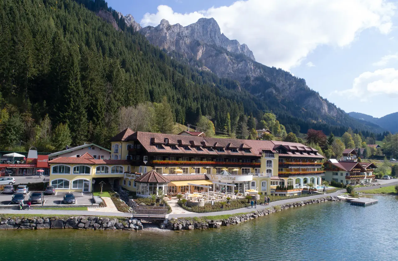 Hotel Via Salina am See mit Bergblick. Idyllische Aussenansicht des Wellnesshotels mit Terrasse und Pool am Seeufer.