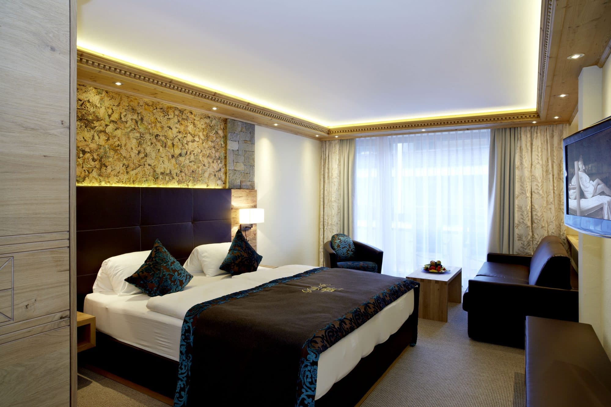 Hotel Tirol Alpin SPA in Ischgl – Komfortables Doppelzimmer mit Sofa und Steinwand-Akzent | Wellnesshotel Tirol