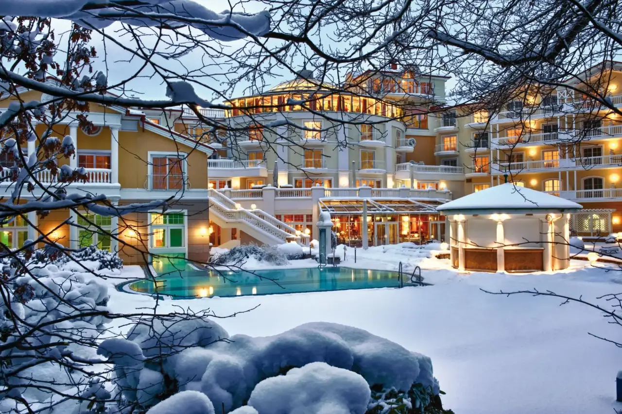 Winterliche Aussenansicht des Travel Charme Strandidyll Heringsdorf mit beleuchtetem Aussenpool und verschneitem Garten.
