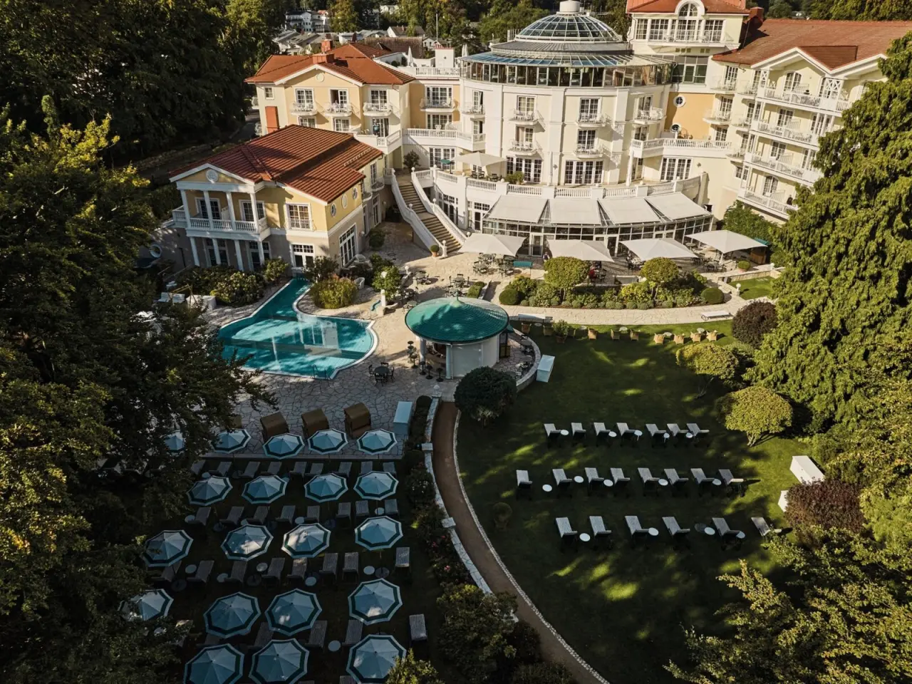Luftaufnahme des Travel Charme Strandidyll Heringsdorf: Hotelgebäude, großer Pool und weitläufige Gärten bei Sonnenschein.