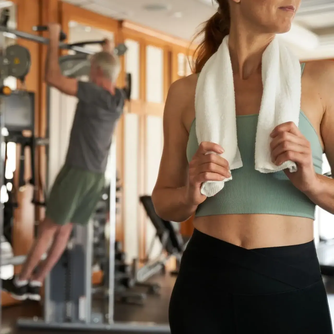Frau mit Handtuch im Fitnessbereich des Travel Charme Strandidyll Heringsdorf. Im Hintergrund trainiert ein Mann.