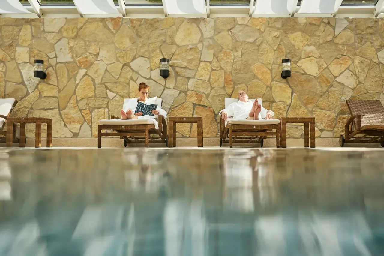 Entspannung am Innenpool mit Steinwand im Travel Charme Strandidyll Heringsdorf. Gäste genießen die Ruhe auf Liegen.