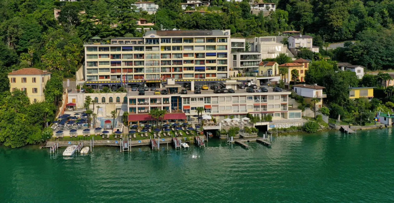 Luftbild des Swiss Diamond Hotel am Luganersee mit Seezugang, Poolbereich und grünen Hügeln im Hintergrund.