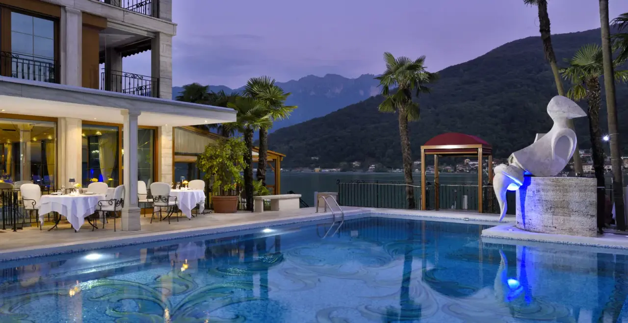Beleuchteter Aussenpool des Swiss Diamond Hotels bei Nacht mit Blick auf den Luganersee und die Berge. Luxuriöses Ambiente.