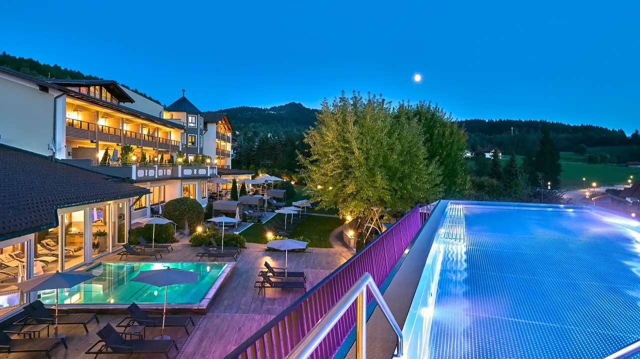 Abendliche Ansicht des Kristall & Vitalhotel Bergknappenhof mit beleuchteten Aussenpools und Gartenanlage unter dem Mond.