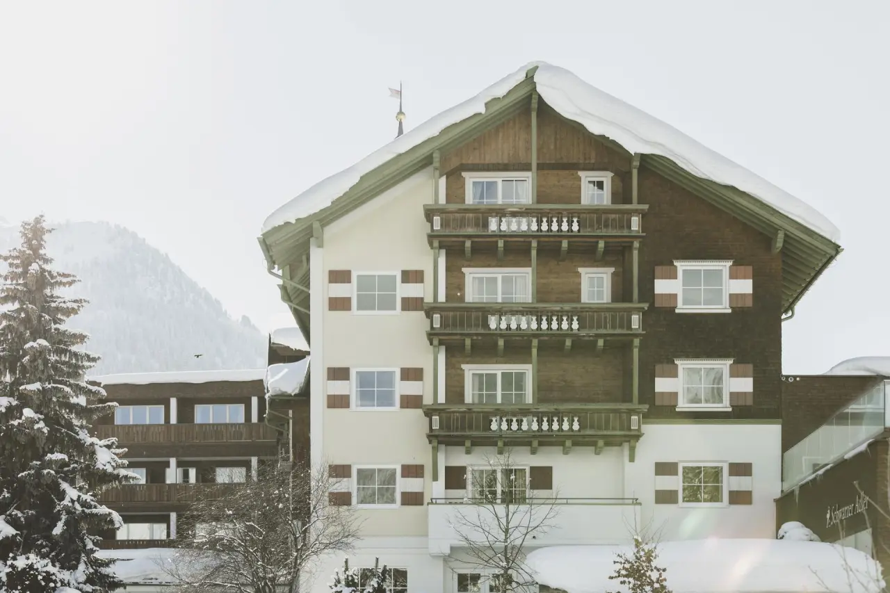 Hotel Schwarzer Adler im Winter: Traditionelle alpine Fassade mit Holzbalkonen und verschneitem Dach vor Bergpanorama.