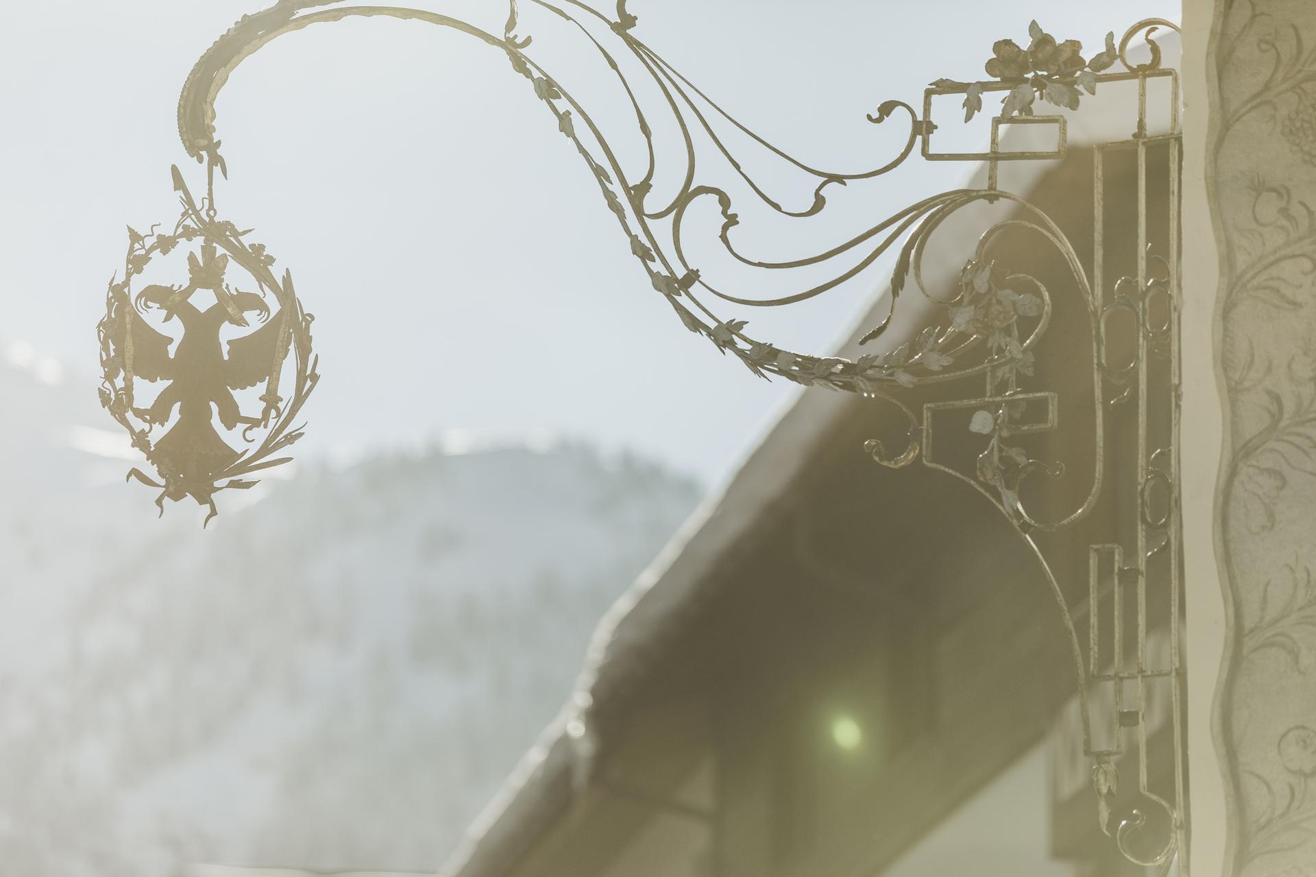 Hotel Schwarzer Adler in St. Anton am Arlberg – Schmiedeeisernes Hotelschild vor Bergkulisse | Wellnesshotel Arlberg