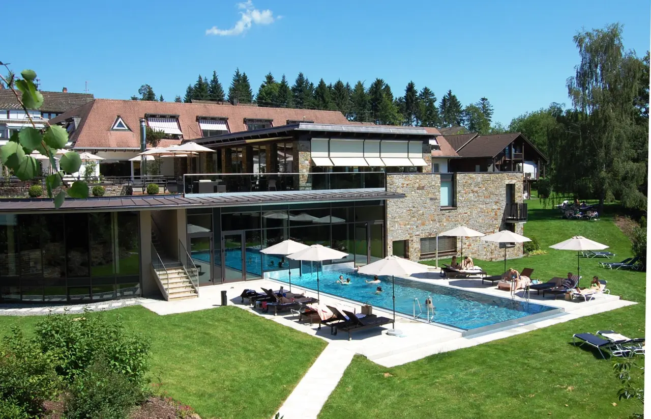 Sonniger Aussenpool mit Liegewiese und Hotelgebäude des Hotel Lauterbad, umgeben von grüner Natur.