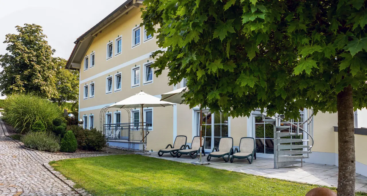Aussenansicht des Landhotels Brandlhof mit sonnigem Gartenbereich, Liegestühlen und grünen Bäumen.