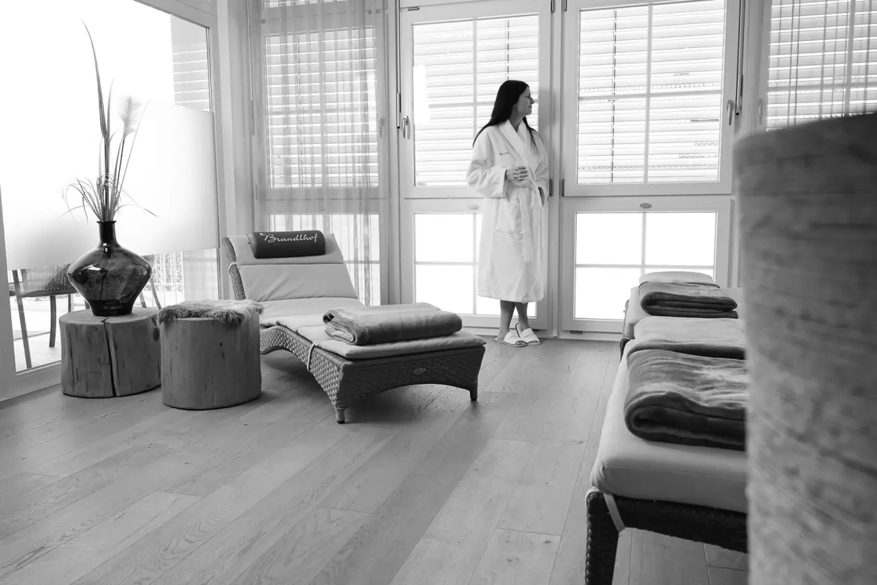 Entspannungsbereich im Spa des Landhotel Brandlhof mit Liegen und Gast im Bademantel am Fenster.