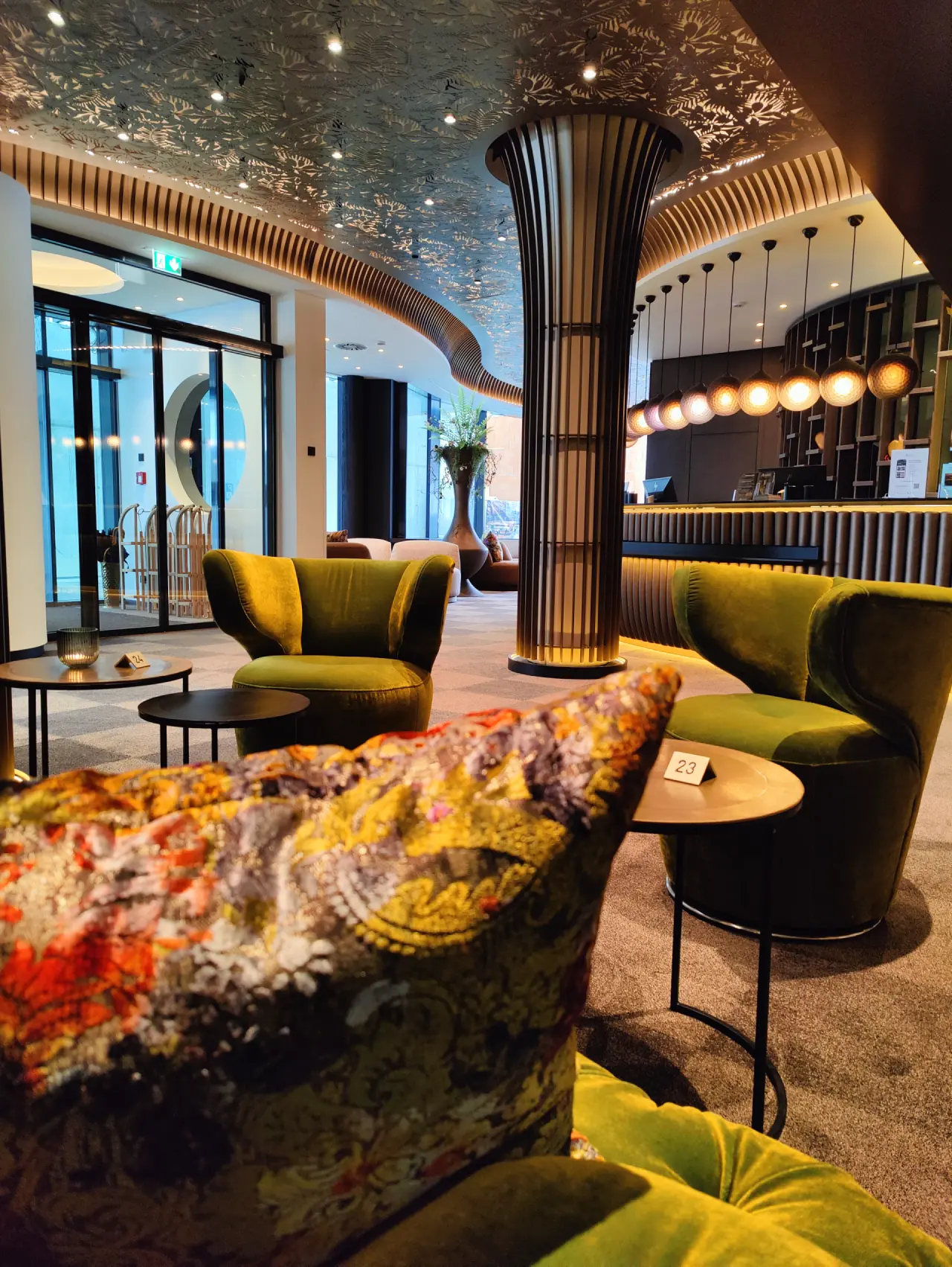 Moderne Lobby des Angerhof Sport- & Wellnesshotels mit grünen Samtsesseln, stilvoller Rezeption und Designer-Decke.