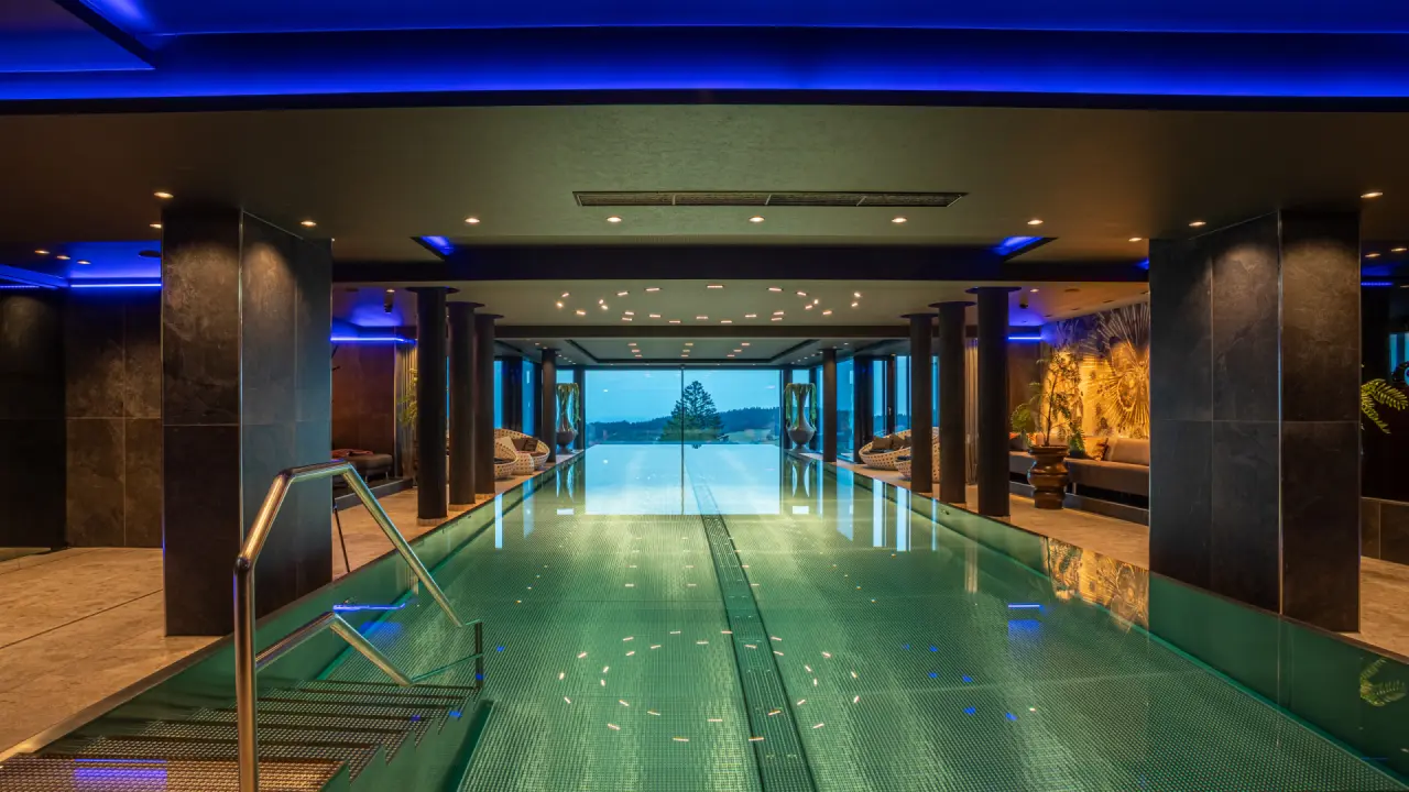 Moderner Indoor-Infinity-Pool mit blauer Beleuchtung und Panoramablick im Angerhof Sport- & Wellnesshotel