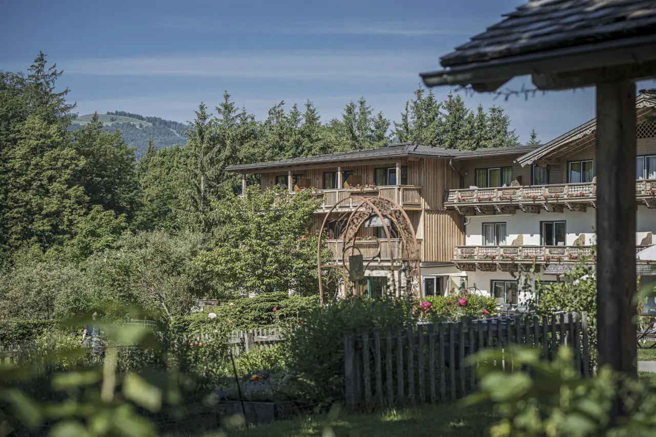 Hotel Bachmanngut in alpiner Umgebung mit traditionellen Holzbalkonen und Blumenkästen, umgeben von grünen Bäumen und Bergen.