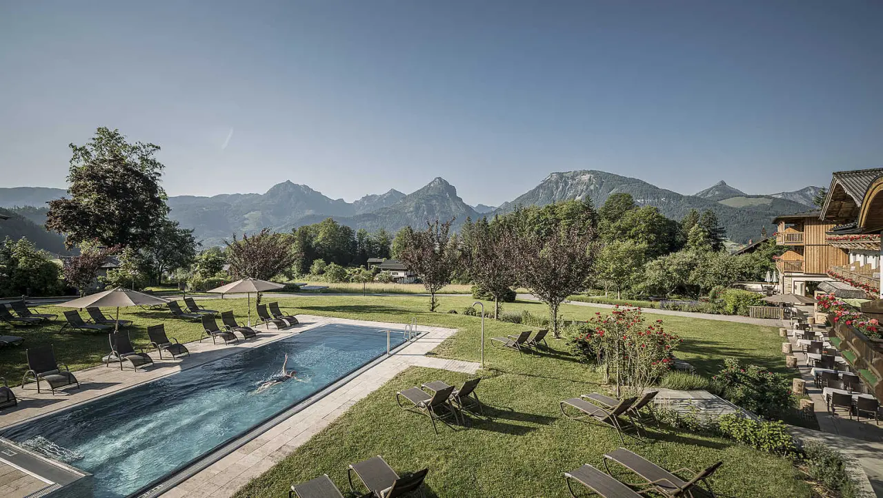Grosser Aussenpool mit Liegestühlen und Sonnenschirmen, umgeben von grüner Natur und majestätischen Bergen im Hotel Bachmanngut.
