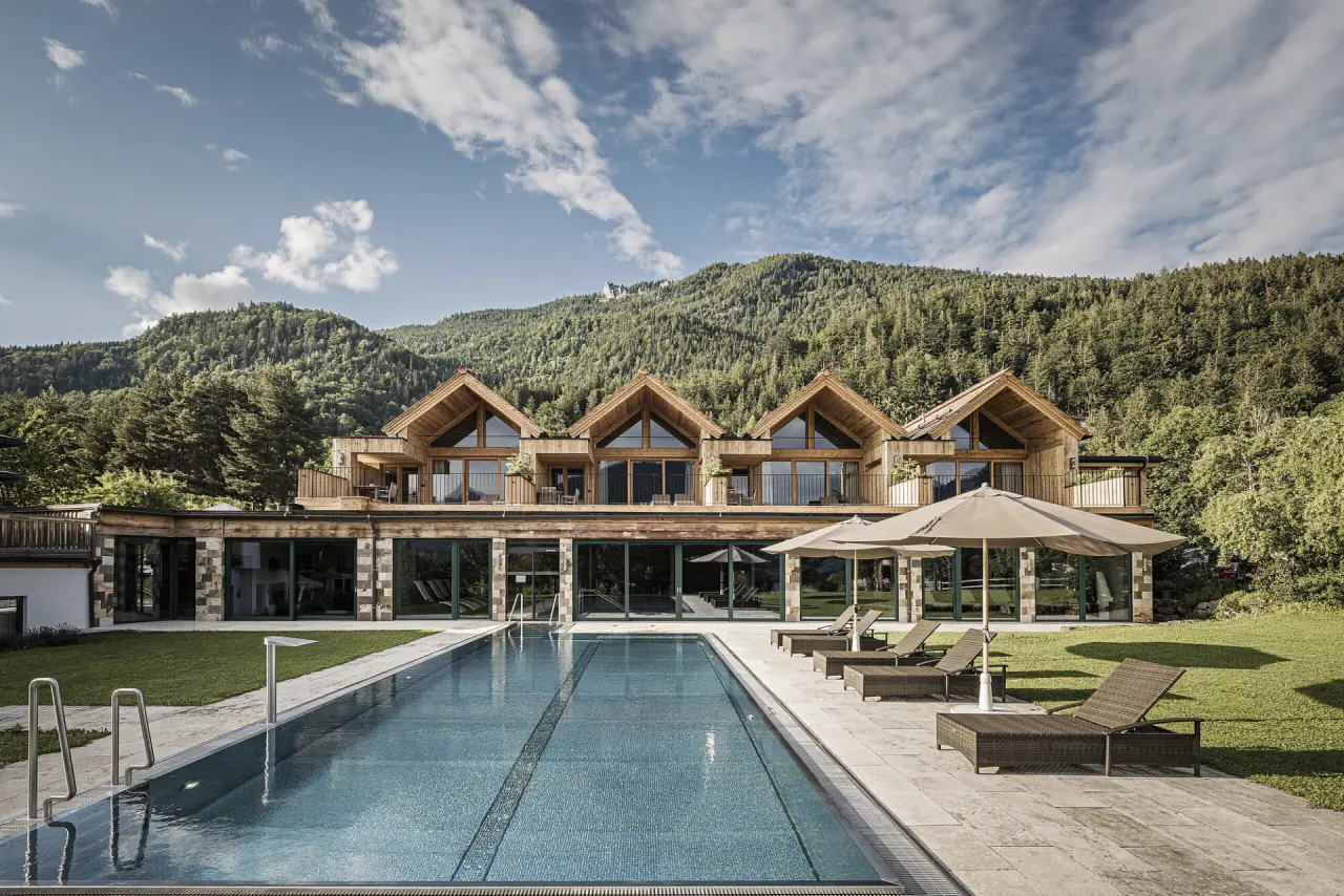 Aussenpool mit Liegen und moderner Holzarchitektur des Hotel Bachmanngut vor idyllischem Bergpanorama.