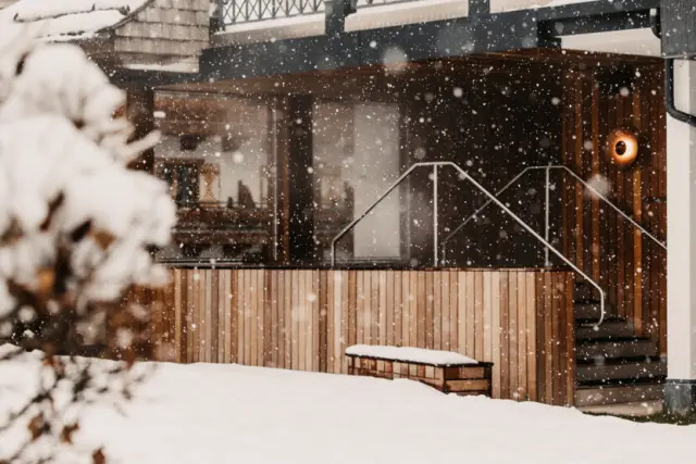 Winterliche Aussenansicht des Hotel Sonnhof Alpendorf mit fallendem Schnee und warmer Beleuchtung am Eingangsbereich.