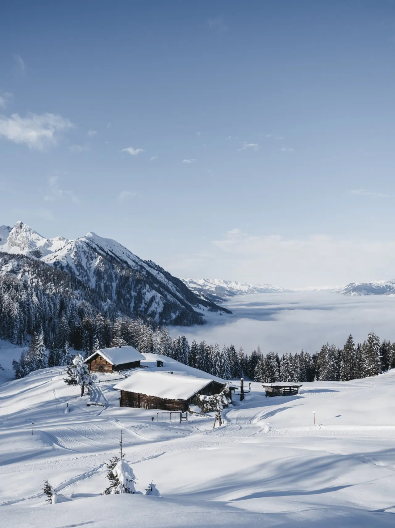 Winterlandschaft mit verschneiten Berghütten und Nebelmeer im Tal, umgeben von schneebedeckten Bergen, Hotel Sonnhof Alpendorf.