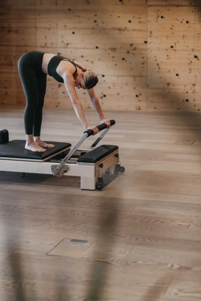 Frau beim Pilates auf einem Reformer im modernen Fitnessbereich des Sonnhof Alpendorf.