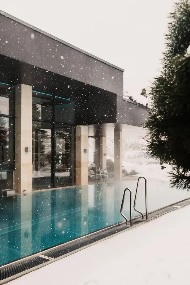 Beheizter Aussenpool im Schnee des Sonnhof Alpendorf. Winterlicher Wellnessbereich mit moderner Architektur und fallendem Schnee.