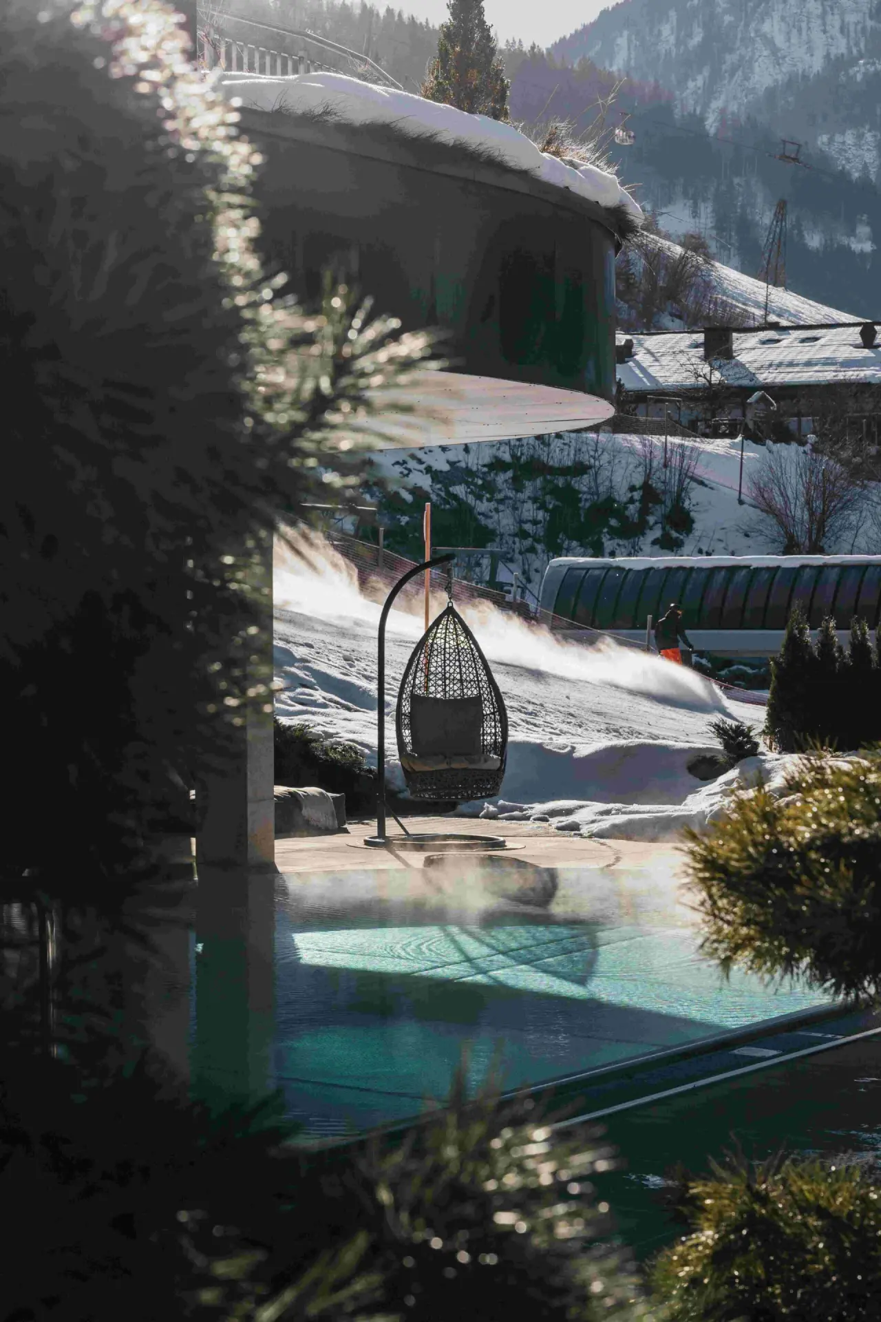 Beheizter Aussenpool mit Dampf und Hängesessel im winterlichen Schnee des Sonnhof Alpendorf. Entspannung mit Bergblick.