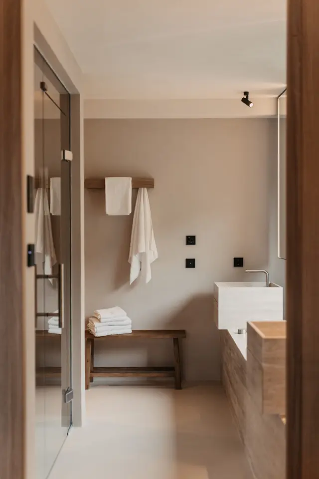 Modernes Badezimmer mit Travertin-Waschbecken, Holzelementen und weissen Handtuechern im Hotel Sonnhof Alpendorf.