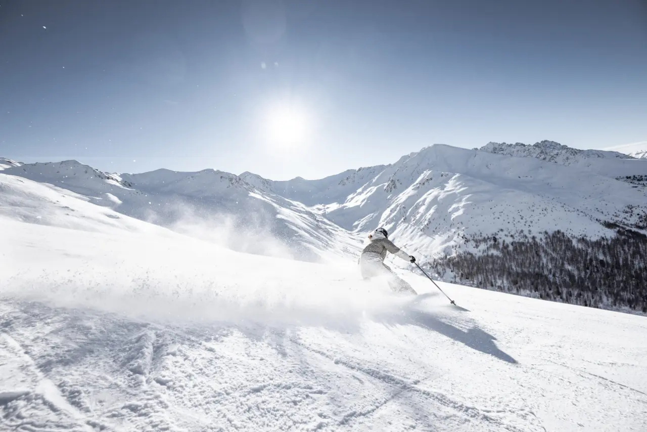 Dynamische Skifahrt im Pulverschnee mit Bergpanorama und Sonnenschein, nahe dem Alpin ART & SPA Hotel Naudererhof.