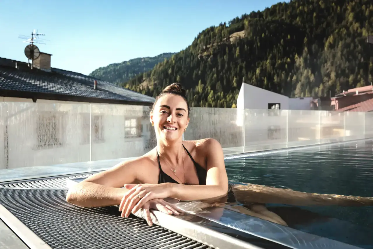 Lachende Frau im Infinity Pool auf der Dachterrasse des Alpin ART & SPA Hotel Naudererhof mit Bergblick.