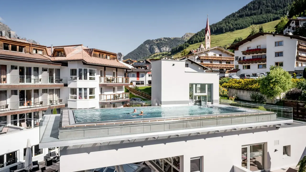 Dach-Infinity-Pool mit Gästen und Panoramablick auf das Bergdorf im Alpin ART & SPA Hotel Naudererhof.