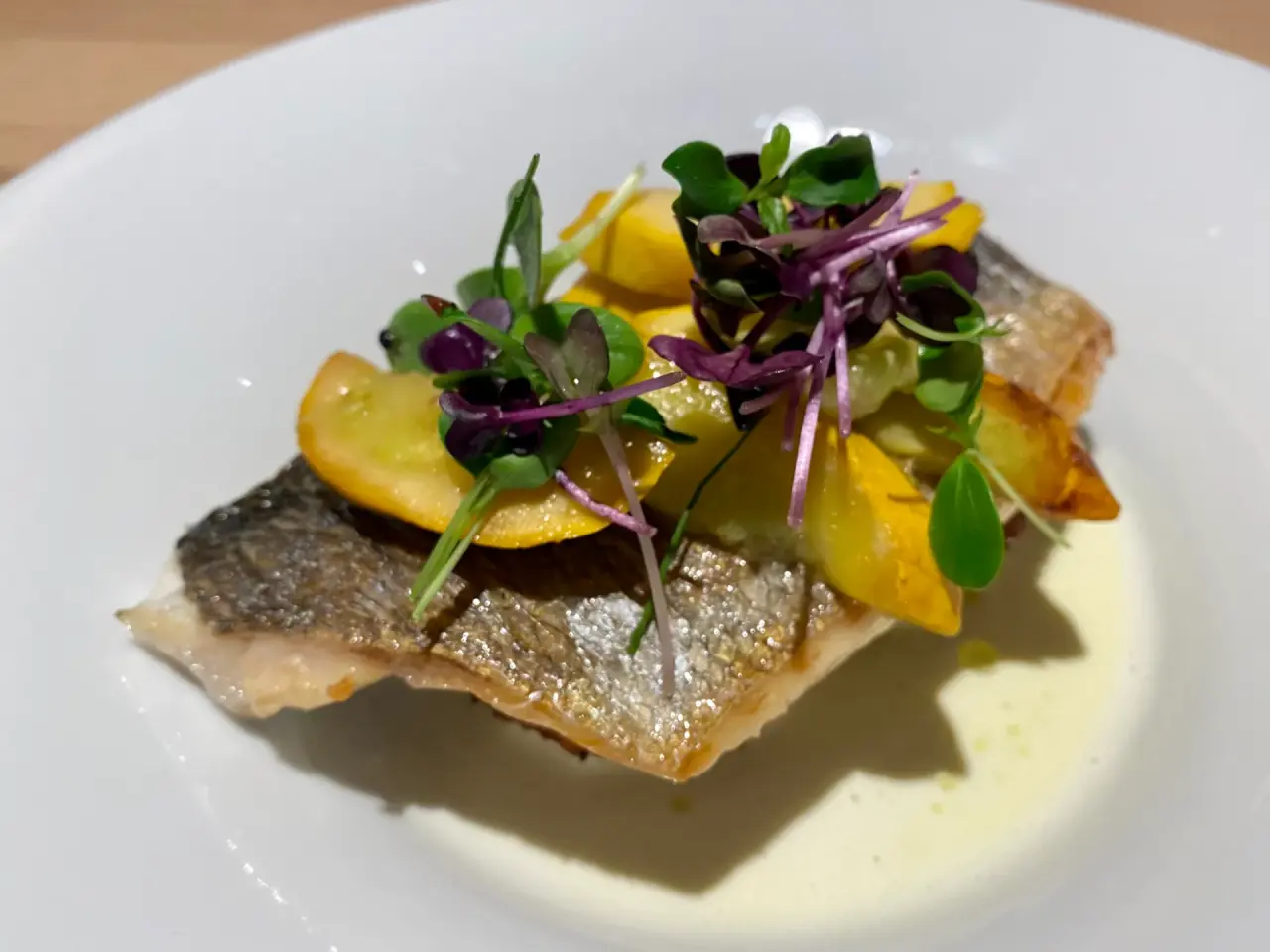 Gebratenes Fischfilet mit gelben Gemüsescheiben und frischen Kräutern auf einem weißen Teller im Alpin ART & SPA Hotel Naudererhof.