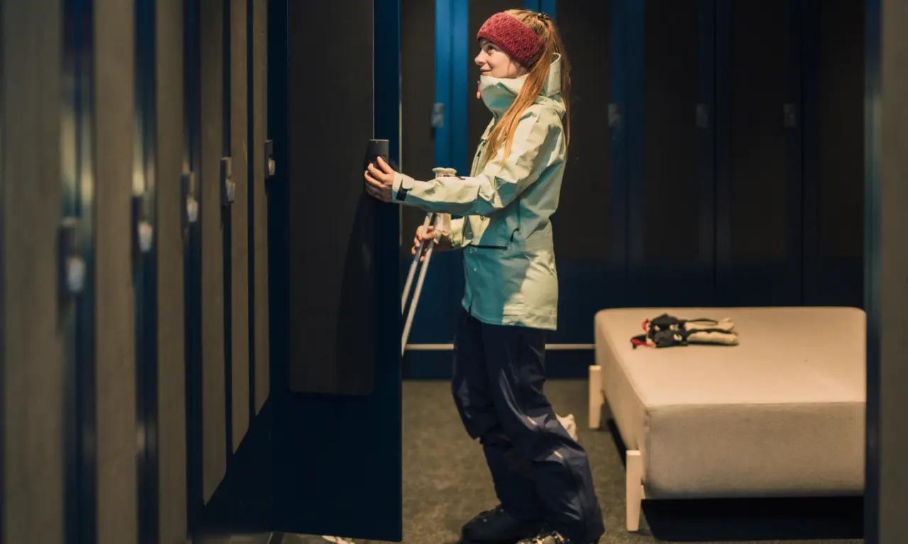 Junge Frau in Skibekleidung schließt Spind im modernen Skiraum der Amrai Suites.