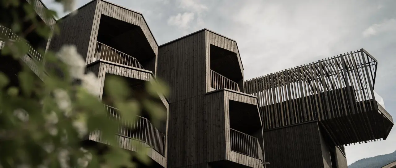 Moderne, dunkle Holzarchitektur der Amrai Suites mit markanten Balkonen und Fassaden, eingebettet in die Natur.