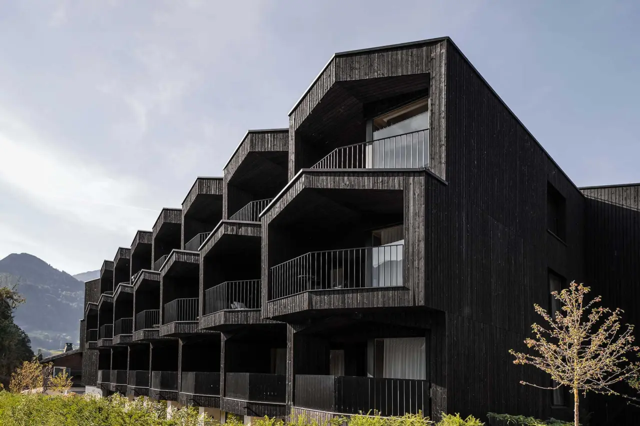 Moderne dunkle Holzfassade der Amrai Suites mit gestuften Balkonen und Bergblick in den Alpen.
