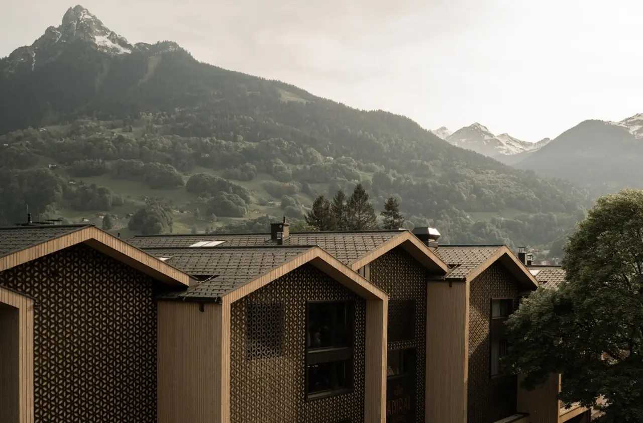Moderne Holzarchitektur der Amrai Suites mit markanten Dächern vor einer beeindruckenden Alpenkulisse.