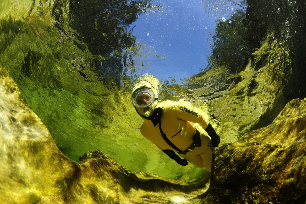 Person in gelbem Tauchanzug beim Schnorcheln in klarem, grünlichem Wasser unter blauem Himmel, Hotel Gasthof Enichlmayr