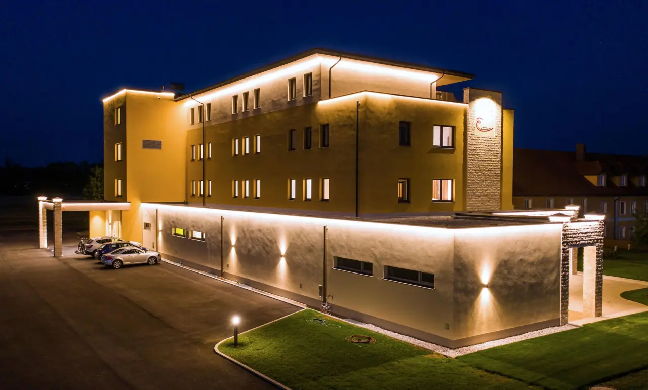 Beleuchtete Aussenansicht des Hotel Gasthof Enichlmayr bei Nacht mit Parkplatz und gepflegter Gruenflaeche.