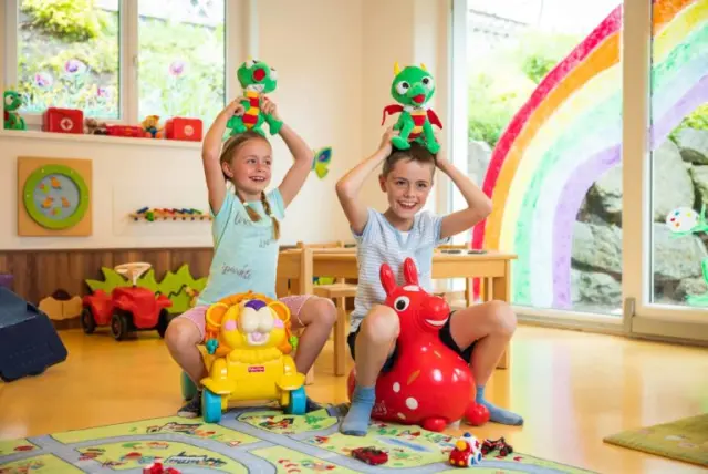 Zwei lachende Kinder spielen mit Stofftieren und Spielzeug in einem bunten Spielzimmer des Alpenpark Resort.
