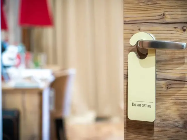 Detailaufnahme einer Holztür mit 'Do Not Disturb' Schild im Alpenpark Resort. Einblick in ein gemütliches Hotelzimmer.