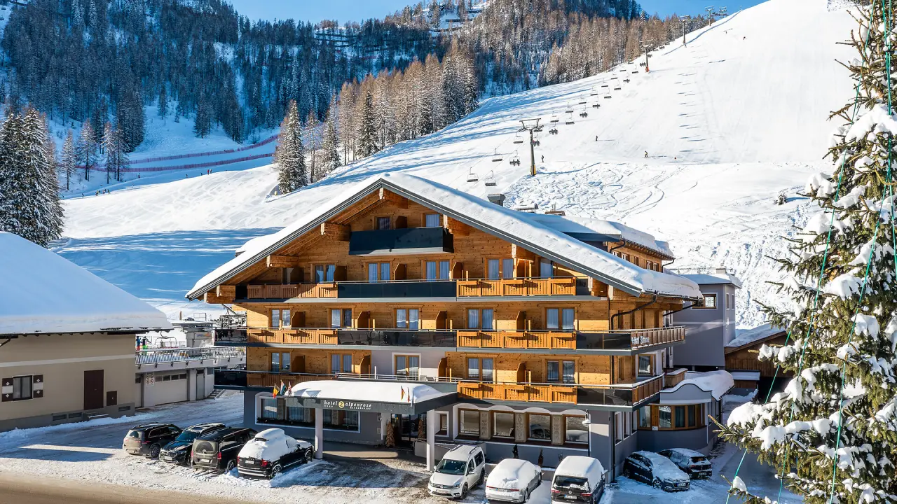 Winterliche Aussenansicht des Hotel Alpenrose direkt an der Skipiste in den verschneiten Alpen unter blauem Himmel.