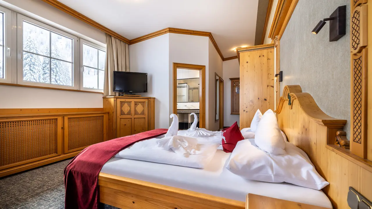 Gemütliches Doppelzimmer im Hotel Alpenrose mit Holzeinrichtung, Blick auf verschneite Landschaft und Badzugang.