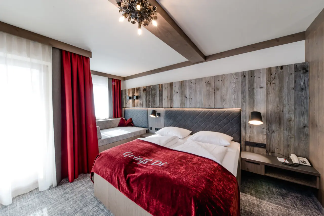 Modernes Doppelzimmer mit Holzelementen, roter Tagesdecke und gemütlichem Sitzbereich im Hotel Alpenrose.