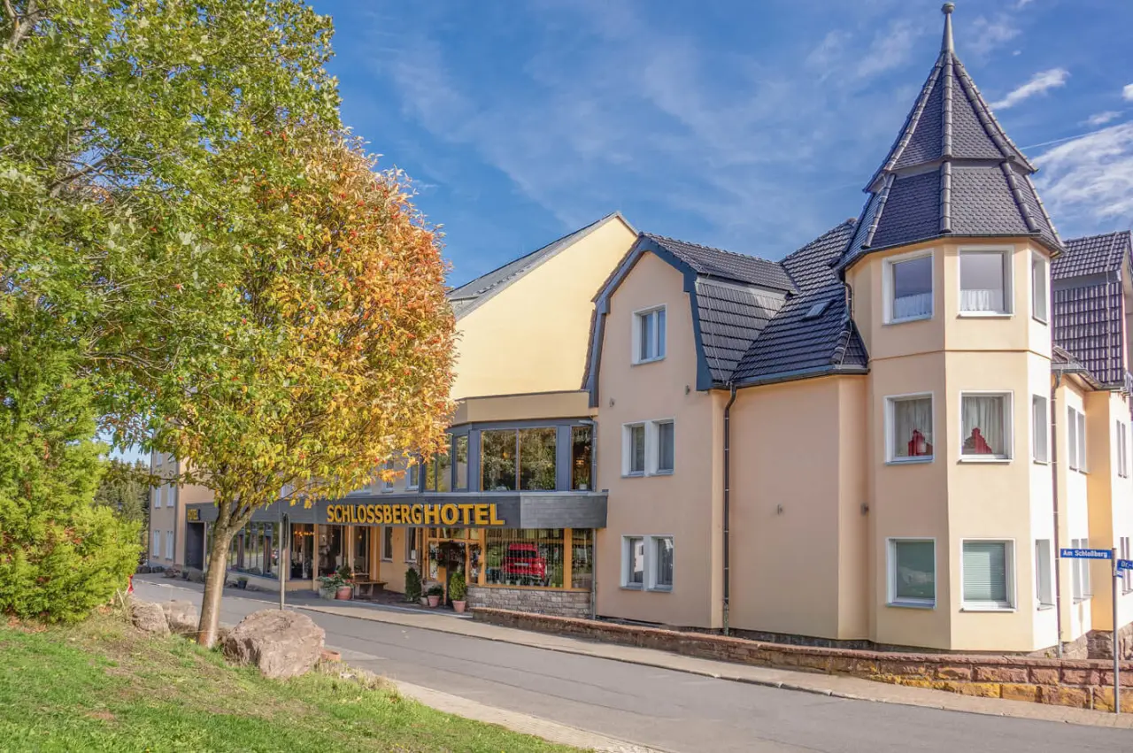 Aussenansicht des Schlossberghotel Oberhof an einem sonnigen Herbsttag mit farbenfrohem Baum und blauem Himmel.