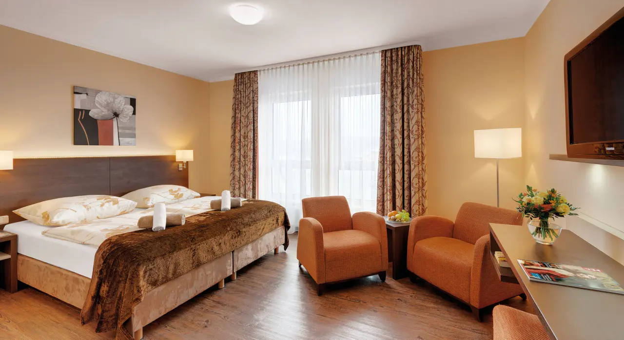 Komfortables Doppelzimmer im Schlossberghotel Oberhof mit gemütlichem Bett, Sitzgelegenheit und Fensterblick.