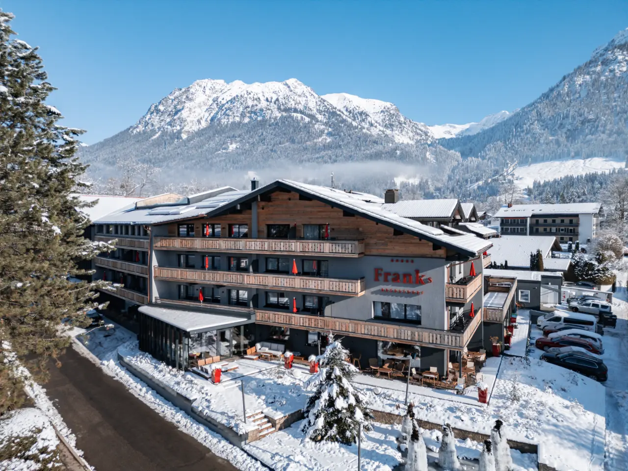 Winterliche Aussenansicht des Hotel Franks in Oberstdorf mit verschneiten Bergen und strahlend blauem Himmel.