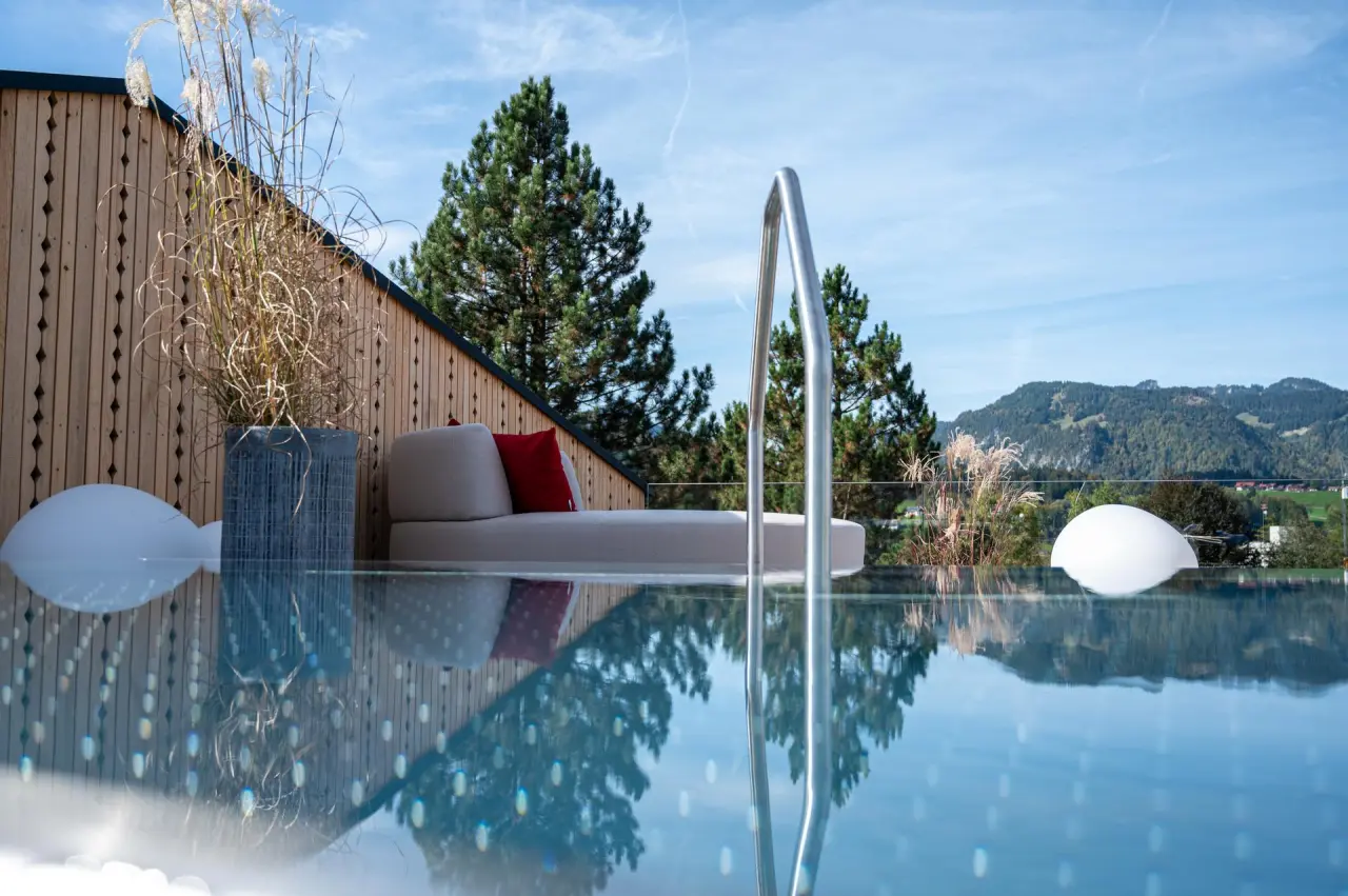 Infinity Pool mit Bergblick und Liegebereich im Hotel Franks. Entspannung unter blauem Himmel.