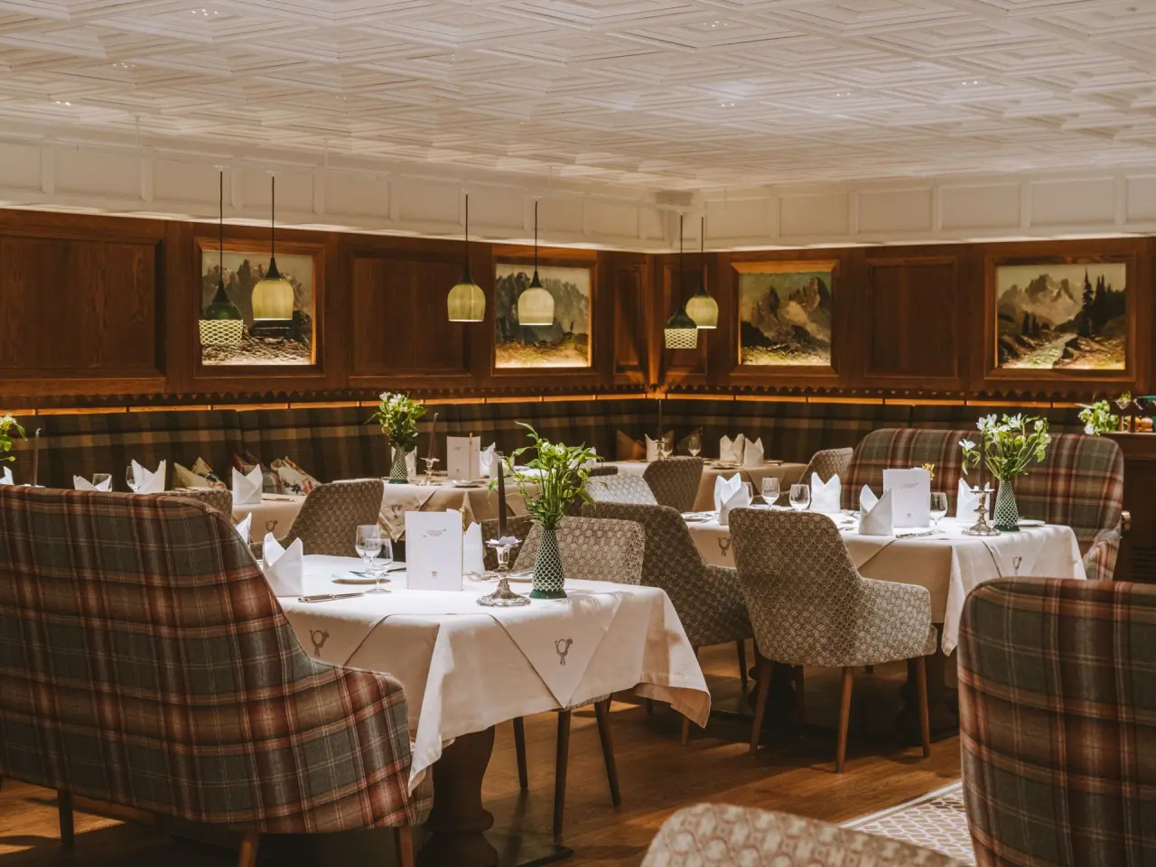 Elegantes Restaurant im Hotel Post Lech mit traditionellem Holzdekor, karierten Sitzbänken und gemütlicher Beleuchtung.