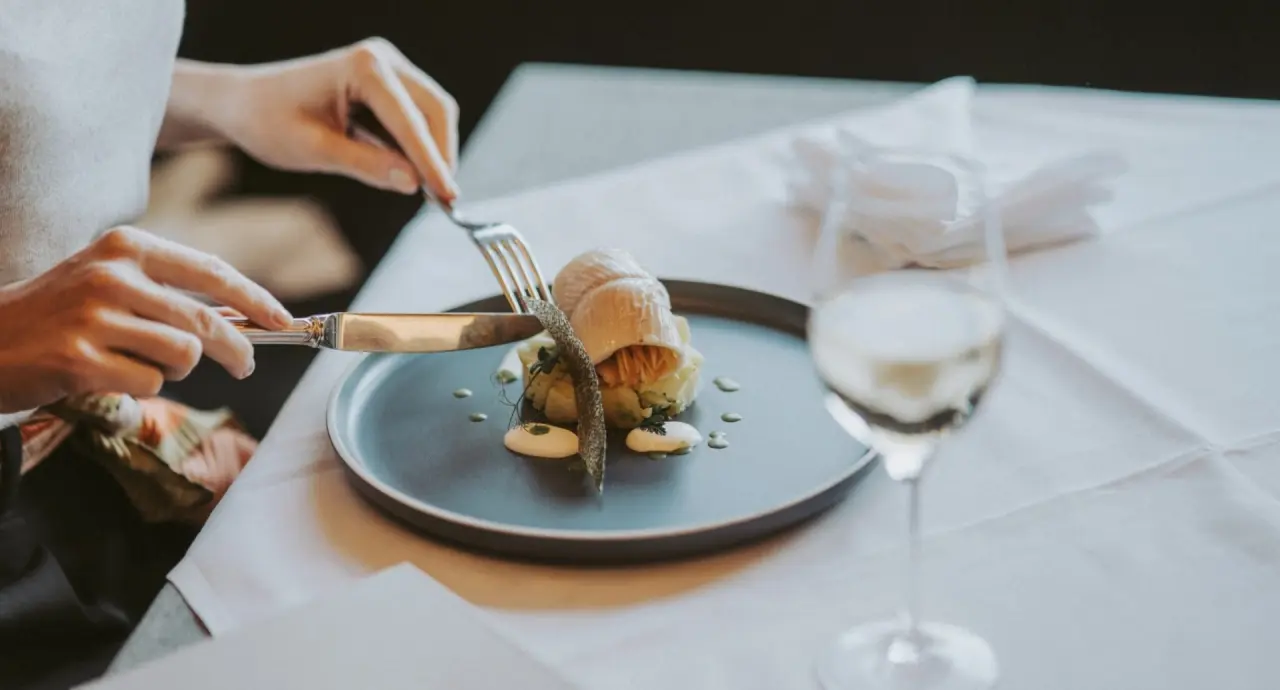 Gast geniesst ein kunstvoll angerichtetes Gericht mit Wein im Restaurant von Mein Hotel Fast.