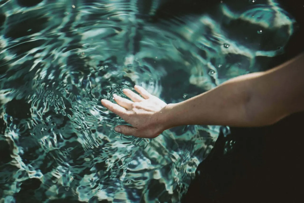 Hand berührt sanft die Wasseroberfläche, erzeugt Wellen. Detailaufnahme für Wellness-Gefühl im Mein Hotel Fast.
