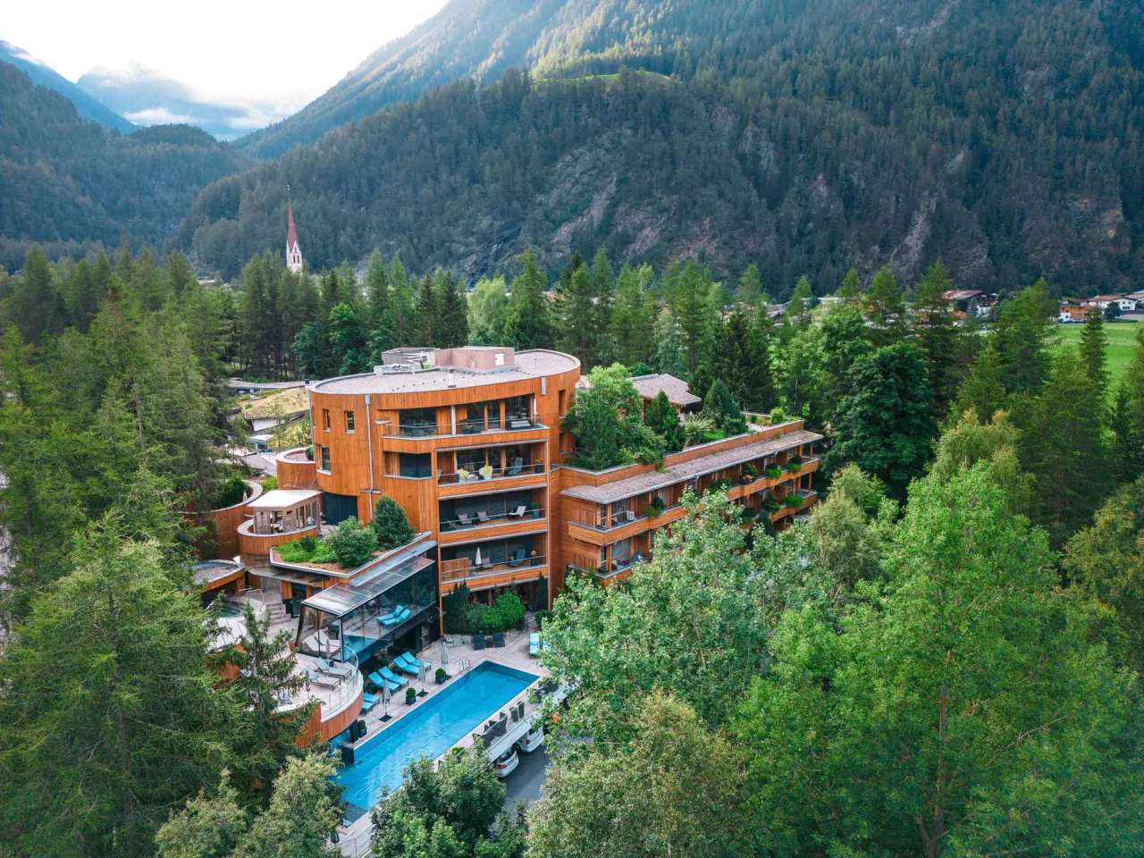 Luftaufnahme des Naturhotel Waldklause mit modernem Holzdesign, Aussenpool und Bergpanorama im Oetztal.