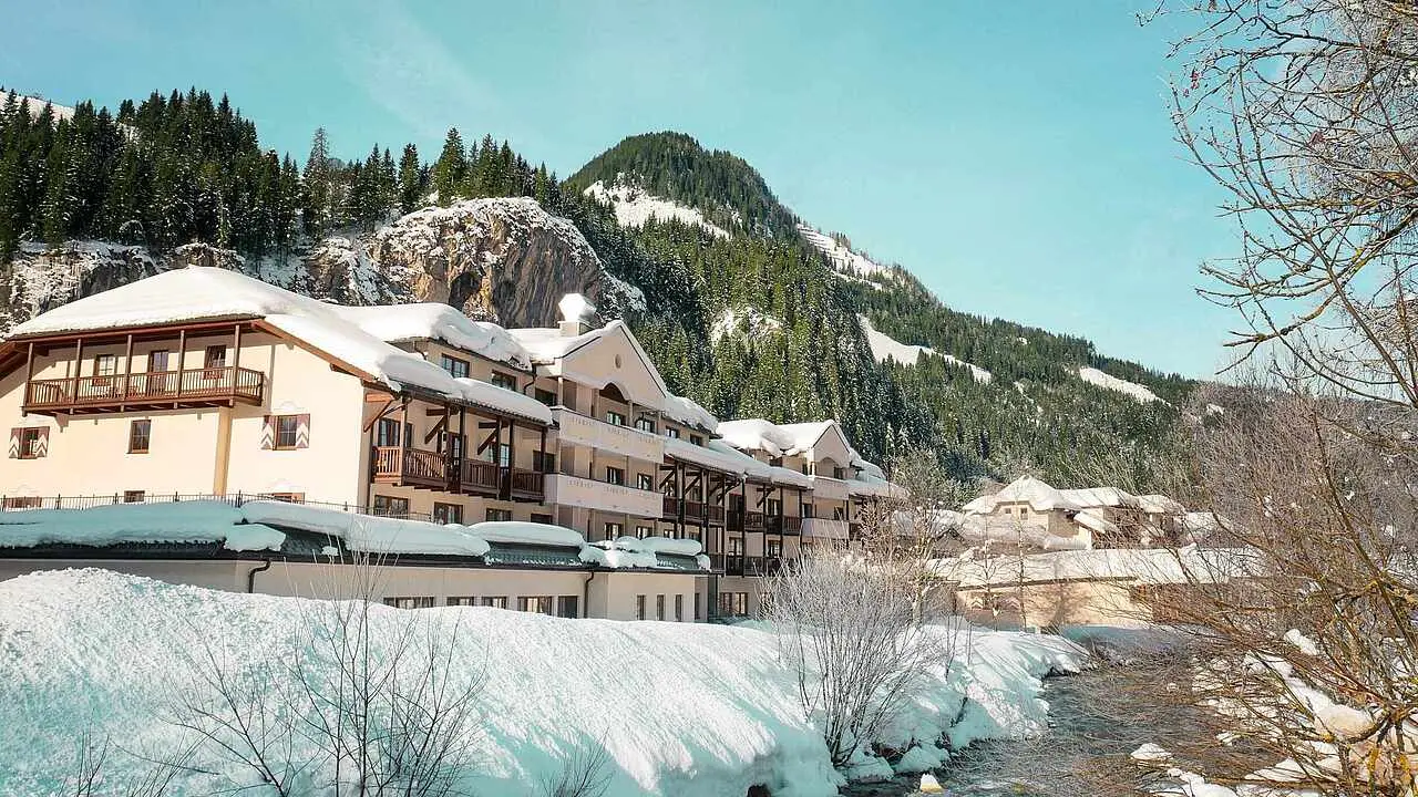 Verschneite Aussenansicht des ROBINSON Amadé Hotels in den österreichischen Alpen, umgeben von Wald und Bergen.